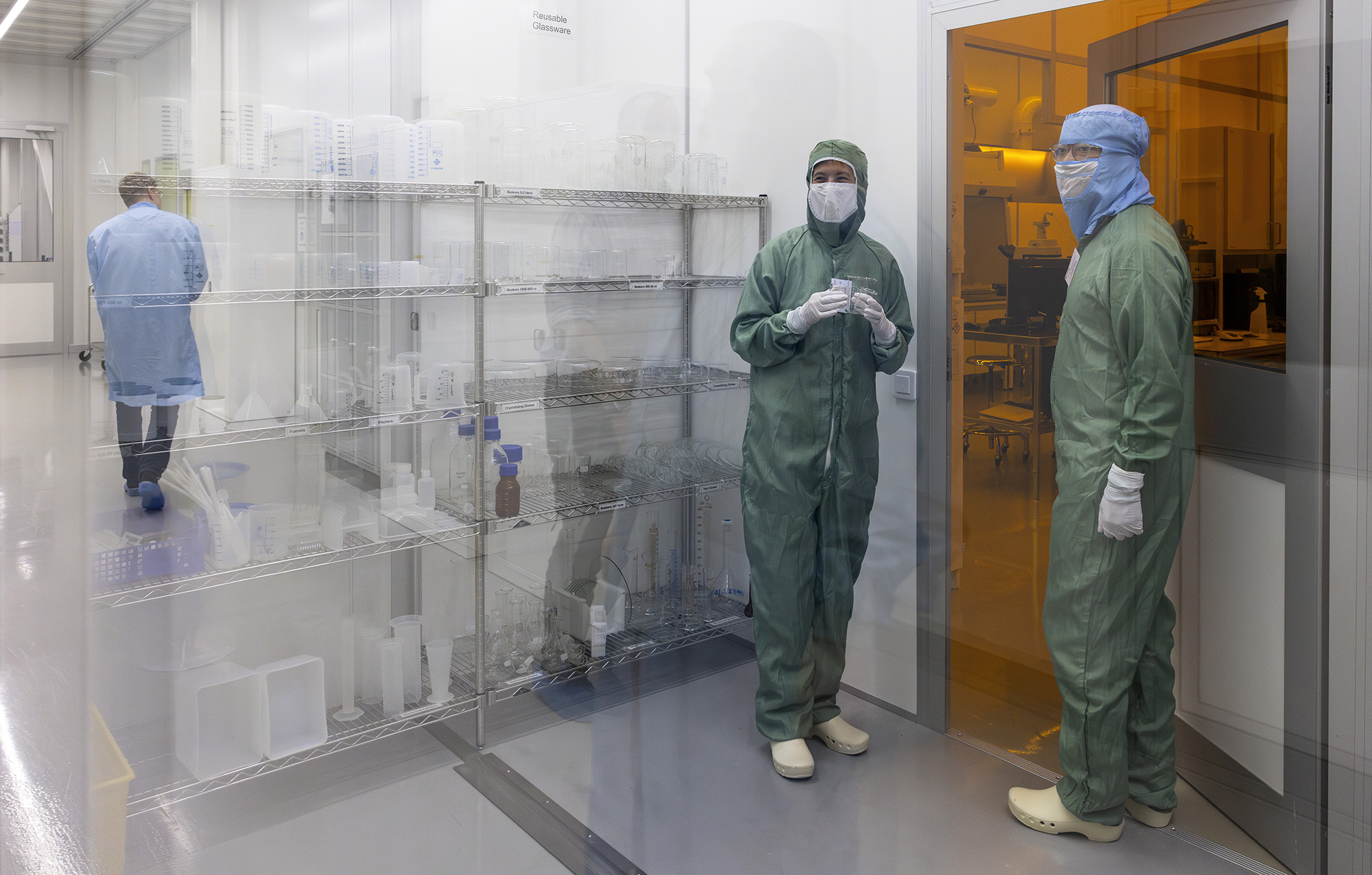 Two people wearing protecting gear on their way to enter a room with yellow dim light.