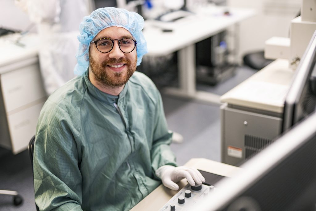 Person in protective gear smiling while sitting down in front of a machine control panel
